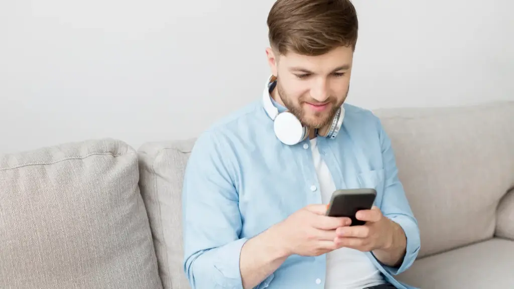 Парень смотрит в телефон и выбирает, что написать девушке в переписке, думая о том, как поднять настроение девушке по переписке и какие фразы из ТОП-40 подойдут лучше всего