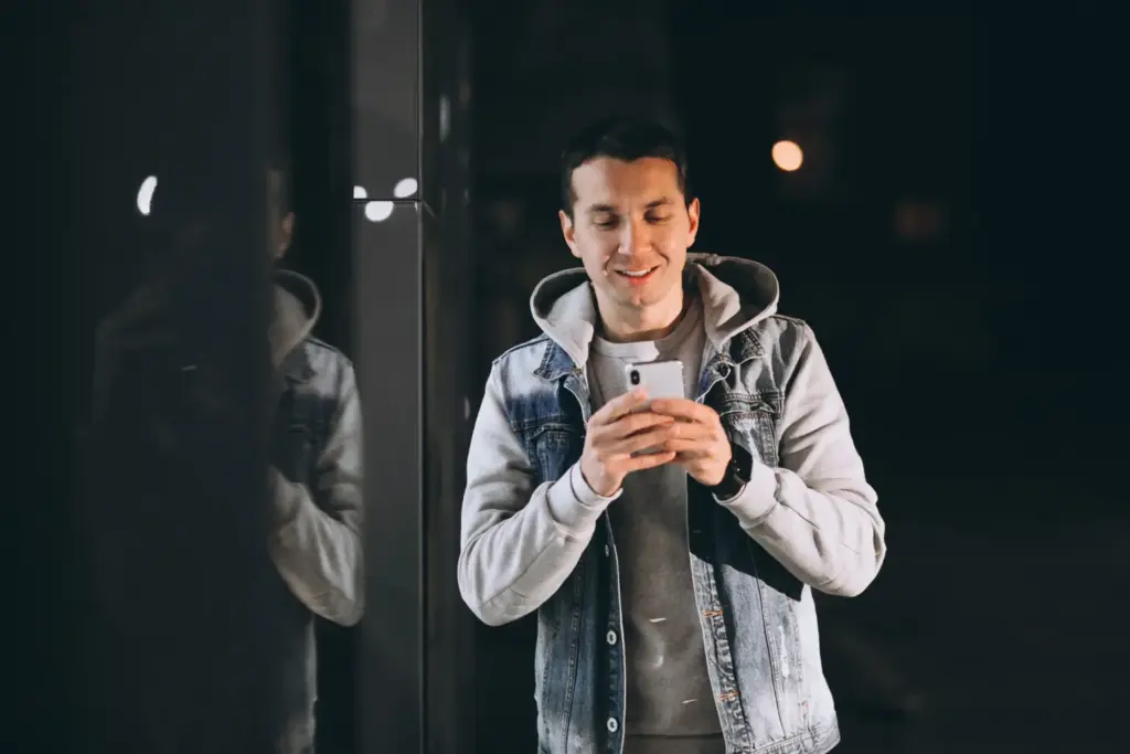 Парень смотрит в телефон и думает, что написать девушке в переписке, выбирая, как начать переписку с девушкой и применяя нестандартные подходы к началу диалога