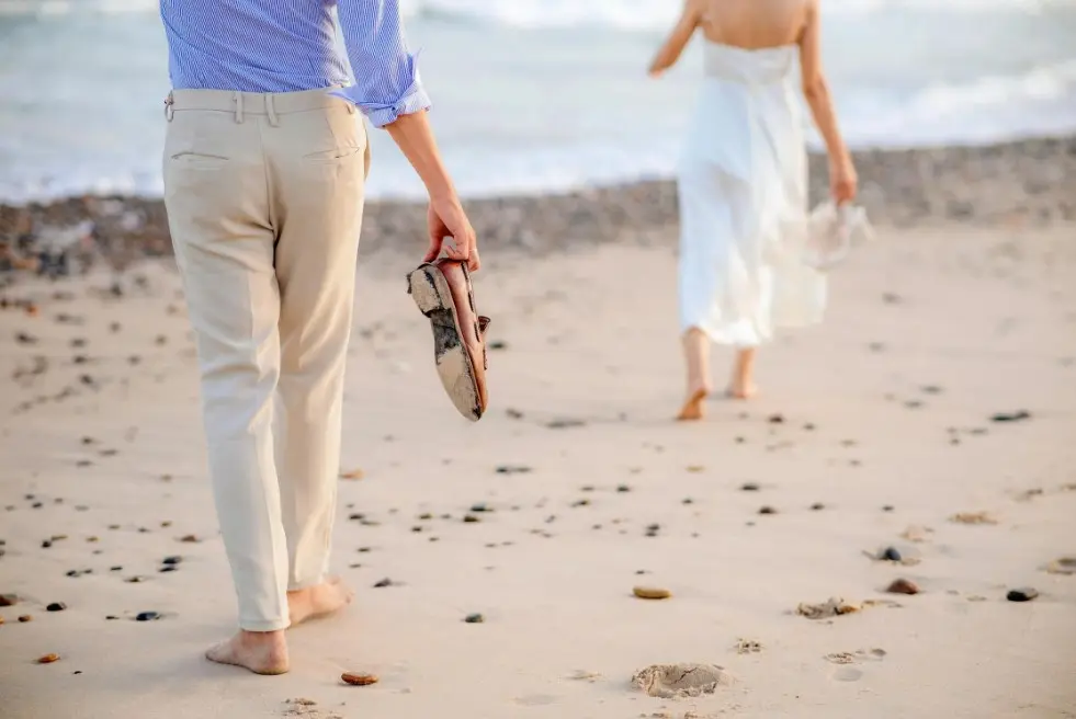 Как устанавливать границы в отношениях — пара идёт по пляжу, мужчина несёт обувь, девушка уходит вперёд вдоль моря