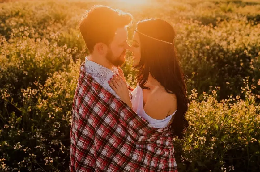 Какие темы нельзя обсуждать на первом свидании: пара обнимается на закате в поле, тёплая романтическая атмосфера
