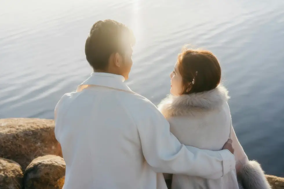 Кто за все платит в паре? Как обсуждать финансовые вопросы — пара в светлой одежде обнимается у воды на закате, спокойствие и доверие.