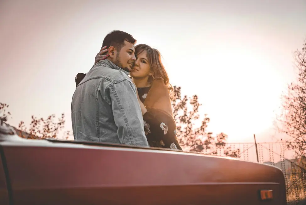 Общаться без намеков и недосказанности — пара обнимается у машины на закате, тёплый романтичный кадр