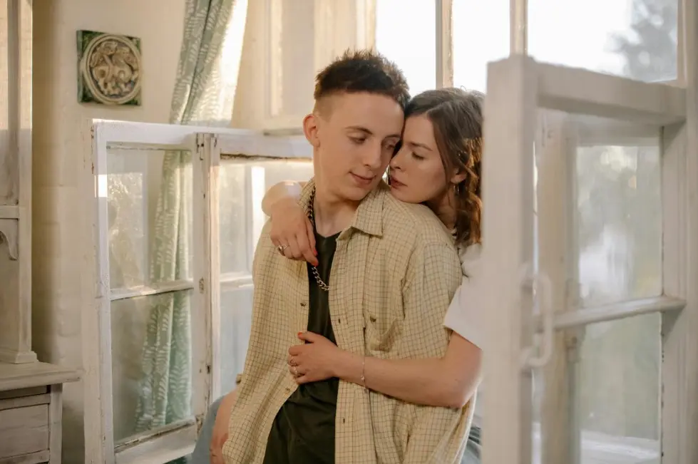 Ошибки в переписке, которые “убивают” интерес — пара обнимается дома у окна, тёплая атмосфера